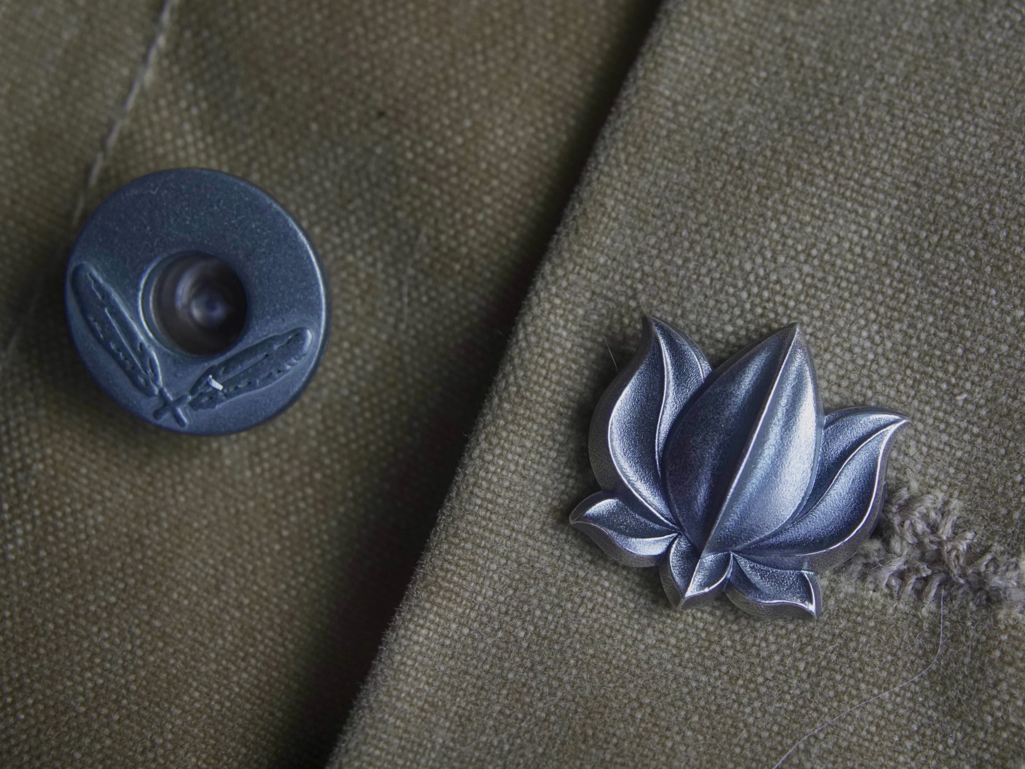 Lotus 001 resting on worn field canvas beside a metal button
