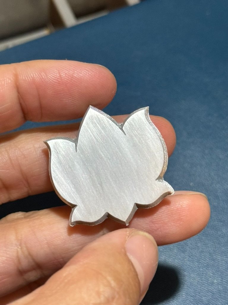 An early lotus prototype held between two fingers, its surface still raw from machining