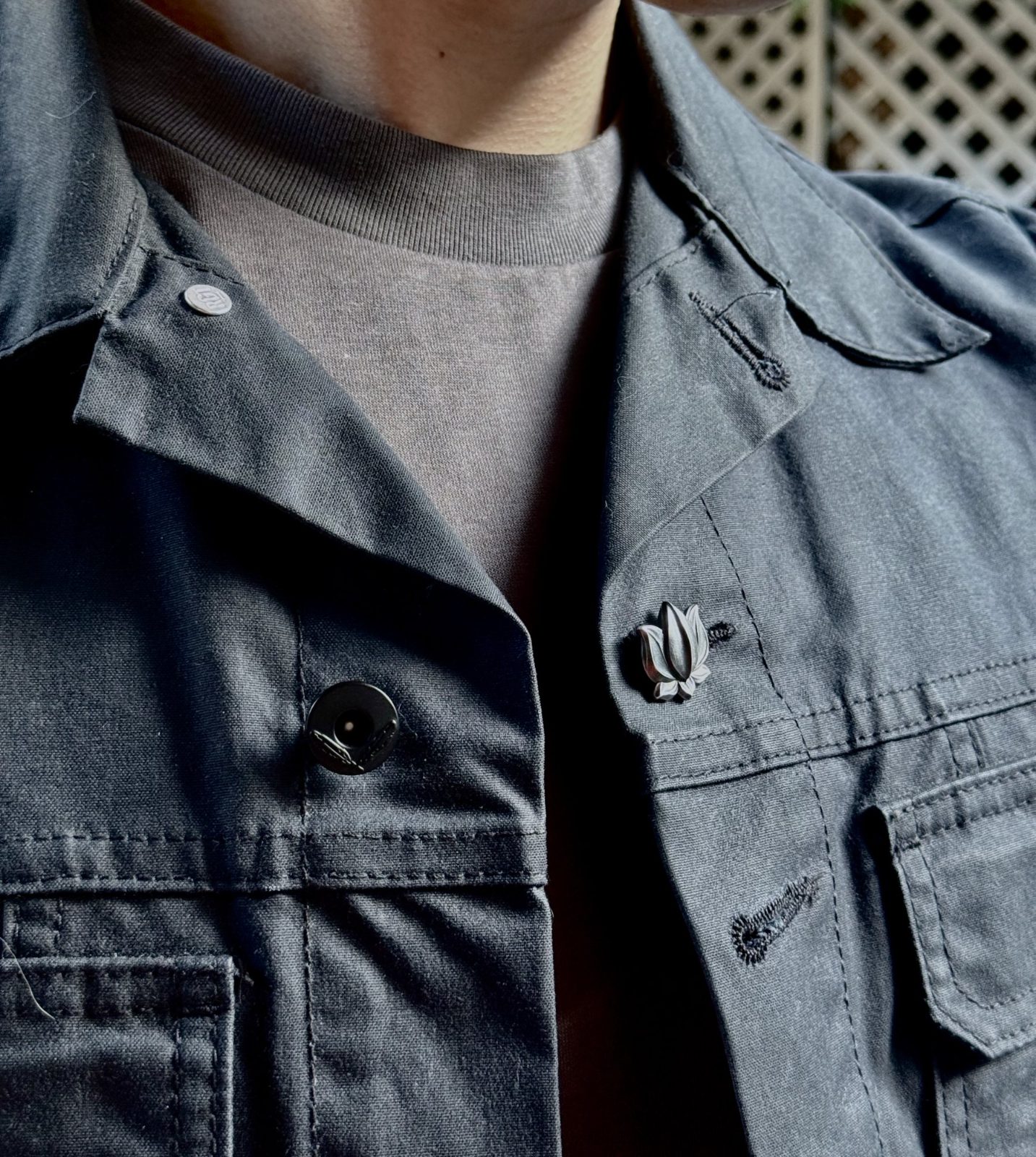 Lotus 001 worn on the chest placket of a grey work jacket
